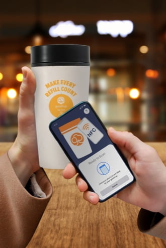 Two hands hold a smartphone in front of a goodcup to scan it.